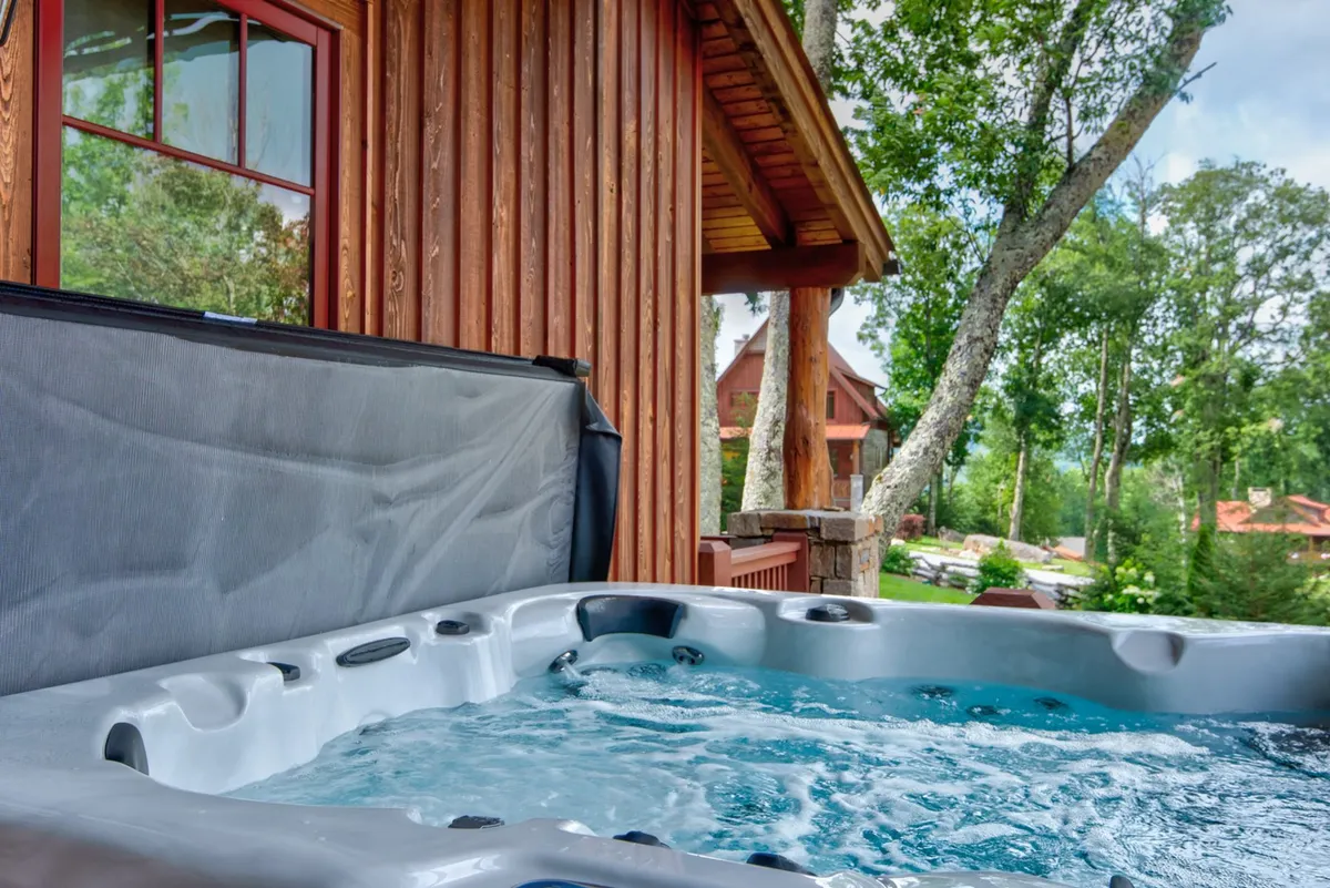 This image features a private hot tub nestled beside a wooden cabin, surrounded by lush green trees. The tranquil setting suggests relaxation and privacy, with a focus on connecting with nature while soaking in the warmth of the tub. The scene is perfect for couples looking for a romantic outdoor escape, with the option to enjoy sunset views and starlit nights.