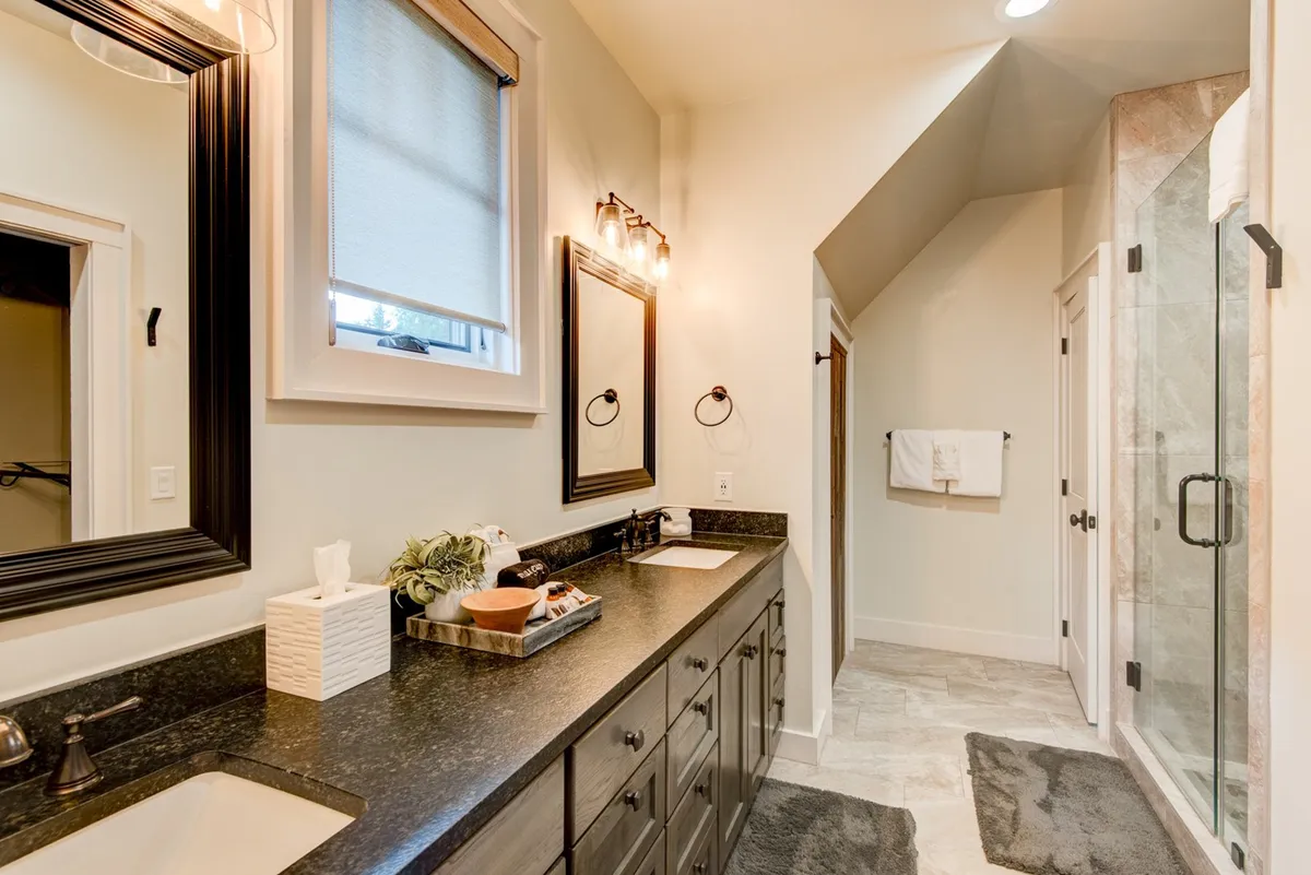 A modern bathroom featuring a double sink vanity with large mirrors and a spacious glass shower enclosure. The space is bright and calming, with spa-like finishes that enhance the sense of rejuvenation and luxury for guests.