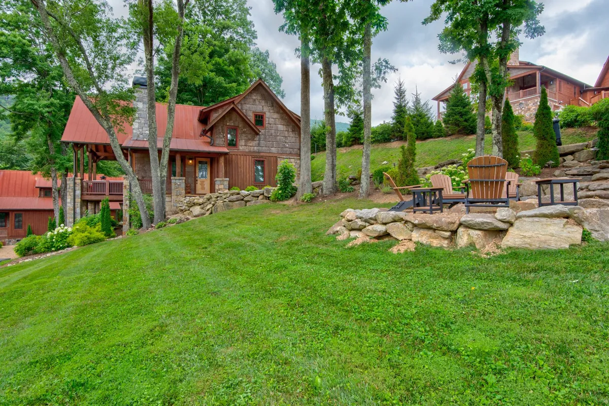 A sweeping view of the main house, Adirondack chairs arranged on a lush green lawn, and mature trees providing a peaceful setting. The arrangement evokes relaxed family gatherings, picnics, and space for children to play—all central to the section’s mention of lawn games, picnics, and community trails.