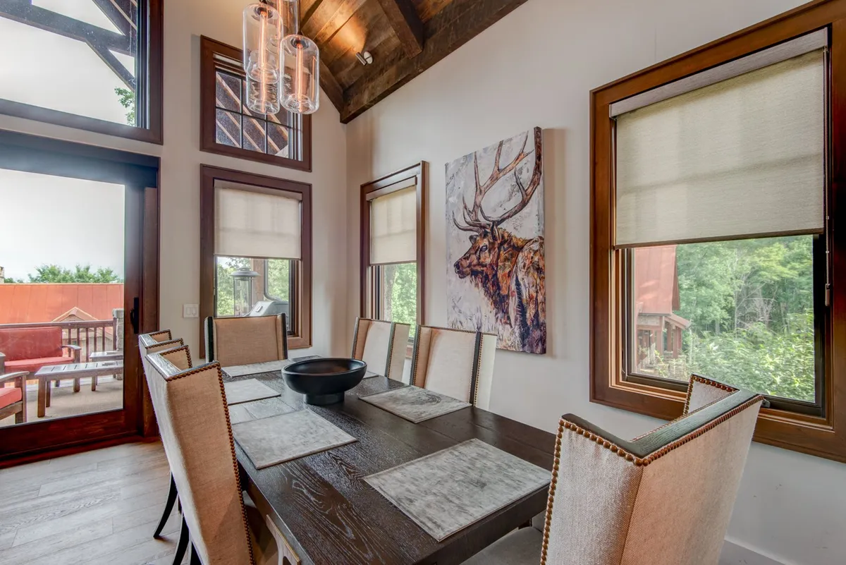 A charming dining area featuring a wooden table set beneath a striking chandelier. Large windows frame views of nature, and an art piece depicting a deer adds local character. The setup is ideal for group meals, intimate dinners, or festive gatherings, with abundant natural light enhancing the ambiance.
