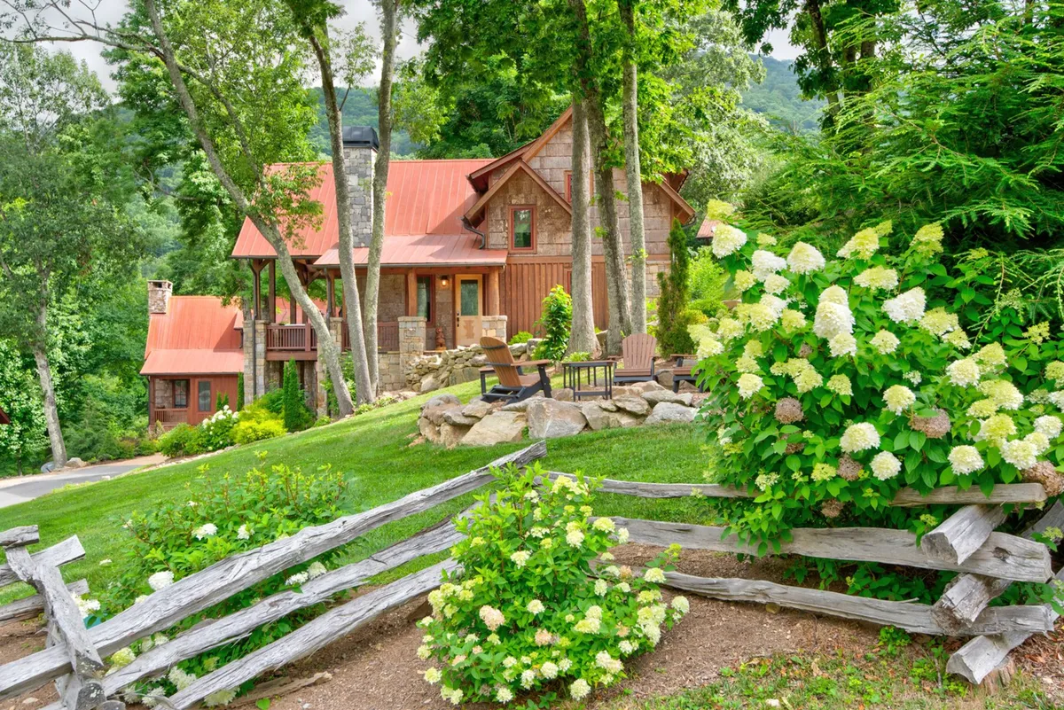 A peaceful exterior setting featuring a rustic house, stone patio, flower beds, and wooden fence, ideal for outdoor dining, stargazing, or enjoying the garden. The tranquil mood and lush garden evoke spring and fall, with opportunities for exploring or relaxing outside.